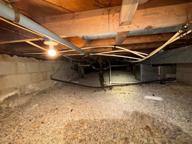 Performed plumbing maintenance inspection in crawl space area, evaluating system pressure via water pressure gauge reading and documenting current mechanical infrastructure conditions. Verified proper PSI levels on pressure regulator and assessed overall plumbing system accessibility and component placement beneath structure.
