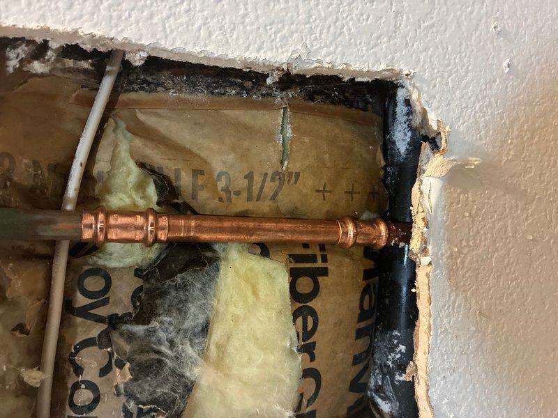 Responded to emergency water leak in basement bathroom caused by accidental pipe penetration during medicine cabinet installation. Upon arrival, assessed damage and located compromised copper water supply line within wall cavity. Created access opening in drywall to expose affected plumbing section. Found punctured copper pipe running horizontally through wall between fiberglass insulation, with active leak point clearly visible. Shut off water supply to affected area and drained remaining water from damaged line. Cut out compromised section of copper pipe and prepared pipe ends for repair. Installed new copper pipe section using soldered joints on both connections to ensure watertight seal. Pressure tested repair to verify integrity of soldered connections and confirm no additional leaks present. Restored water supply and conducted final inspection to ensure proper flow and system operation.