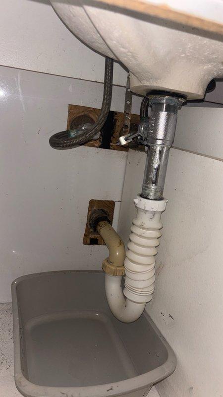 Responded to bathroom sink with reported drainage issues and leak beneath the fixture. Upon inspection, found corroded P-trap assembly and deteriorated drain connections causing both the blockage and leak. Customer had previously attempted to clear the drain with chemical drain cleaner multiple times, which contributed to the deterioration of the plastic components. Removed and replaced the defective P-trap assembly with new white plastic P-trap and corrugated flexible drain pipe. Installed gray drip basin beneath the plumbing assembly to protect cabinetry. Tested the drain system for proper flow and verified all connections were secure with no leaks present.
