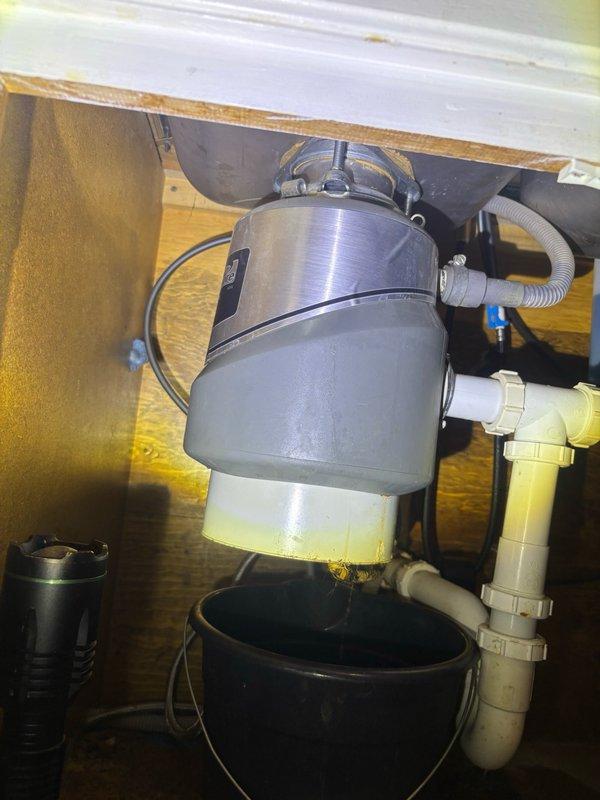 Responded to service call for garbage disposal leak and clogged drainage system affecting kitchen and bathroom fixtures. Upon inspection, identified active leak from garbage disposal unit with visible yellow discharge into containment bucket. Assessed P-trap configuration and disposal mounting assembly for integrity issues. Addressed clogged drainage in bathroom sink and kitchen plumbing system. Cleared blockages from waste lines, inspected disposal unit connections and mounting flange for proper seal, and verified P-trap assembly for debris accumulation. Documented existing water damage on cabinet floor indicating previous leakage issues. Tested drainage flow through garbage disposal and connected waste lines to ensure proper function and eliminate backup conditions.