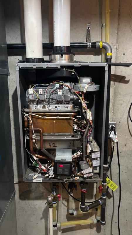 Responded to service call for non-operational tankless water heater in basement that had been previously disassembled by another plumber. Upon arrival, found 11-year-old gas-fired tankless unit with front panel removed and internal components exposed, including heat exchanger, gas burner manifold, copper water circulation piping, and electrical connections. Performed thorough assessment of unit condition and photographed existing installation showing PVC exhaust venting, yellow flexible gas supply lines, shut-off valves, and various connection points. Evaluated whether unit could be repaired or required full replacement. Explained difference between estimate service and diagnostic service call, with customer agreeing to proceed with comprehensive evaluation to determine most appropriate course of action for restoring hot water service.