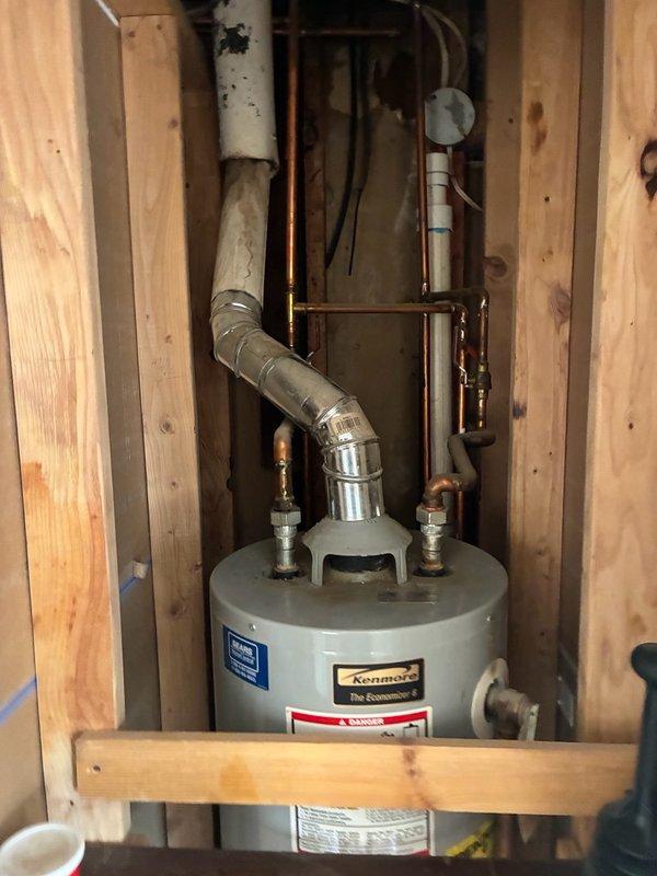 Conducted on-site assessment of 20-year-old Kenmore slim water heater located in basement utility closet. Unit currently operational but homeowner requested preventative replacement estimate following recent property purchase. Inspected existing installation including inlet/outlet plumbing connections, copper supply lines with shutoff valves, metallic flue pipe configuration, and overall equipment condition within confined closet space. Documented equipment specifications, mounting configuration, and surrounding plumbing infrastructure to provide accurate replacement recommendations and pricing for slim-profile water heater suitable for tight installation space.