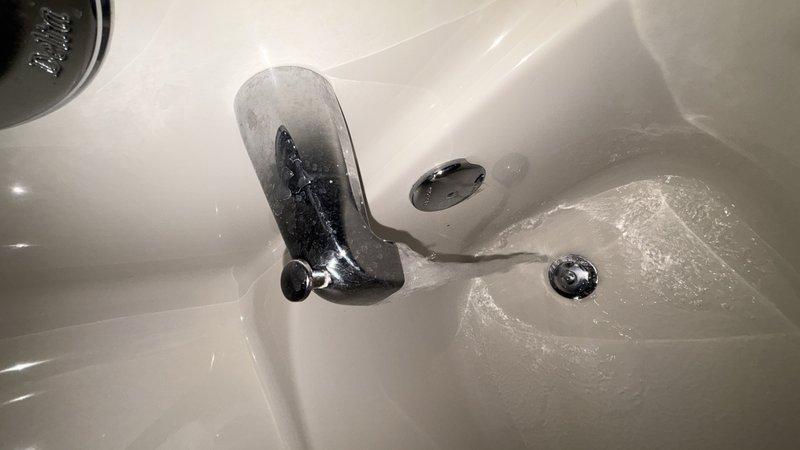 Completed comprehensive whole home plumbing inspection examining all accessible fixtures and components. Documented condition of bathroom fixtures including shower valve assembly with chrome finish showing mineral deposit accumulation and water spotting, and porcelain sink with single-lever chrome faucet, verifying proper drainage function through main and overflow drain openings.