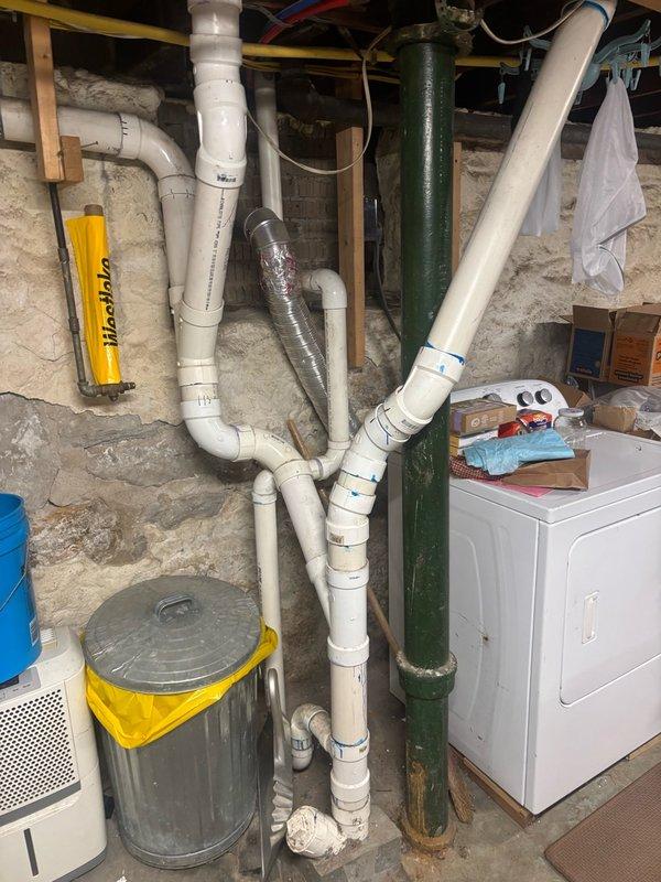 Responded to basement drainage issue and house trap replacement request. Upon inspection, assessed the plumbing system including the existing house trap configuration, PVC drain lines, and cast iron waste stack in the basement utility area. Evaluated the clogged drain condition and determined necessary repairs to restore proper drainage function. Documented existing plumbing infrastructure with photographic evidence showing the network of waste and vent piping, connections, and overall system layout for repair planning and customer records.
