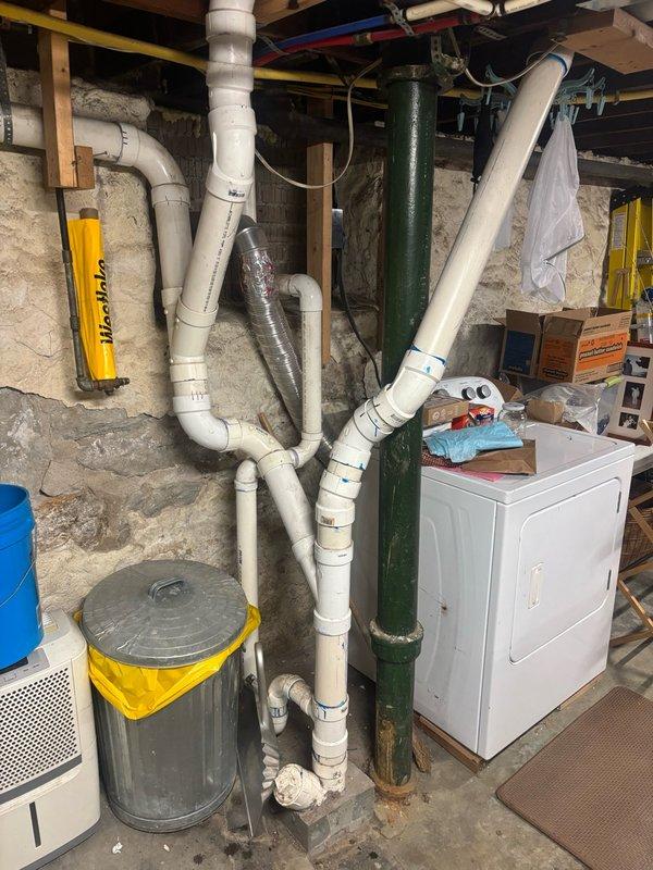Responded to basement drainage issue and house trap replacement request. Upon inspection, assessed the plumbing system including the existing house trap configuration, PVC drain lines, and cast iron waste stack in the basement utility area. Evaluated the clogged drain condition and determined necessary repairs to restore proper drainage function. Documented existing plumbing infrastructure with photographic evidence showing the network of waste and vent piping, connections, and overall system layout for repair planning and customer records.