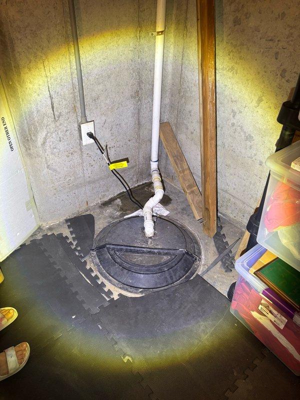 Responded to service call for sump pump activating but water pooling adjacent to unit in sub basement. Upon inspection, found existing sump pump system with visible mineral deposits and sediment accumulation throughout pit. Pump was cycling on as reported, but discharge system required evaluation due to water backup. Assessed PVC discharge piping, pump float mechanism, and check valve operation. Pit showed signs of age with heavy buildup on walls and standing water at base. Documented existing conditions including pump assembly, electrical connections, and discharge plumbing configuration for repair recommendations.