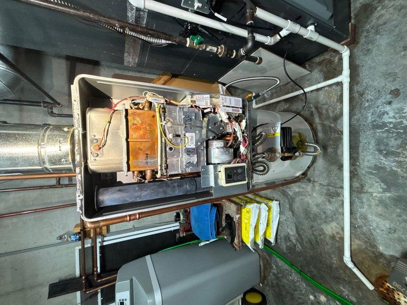 Completed plumbing maintenance visit inspecting bathroom fixtures and mechanical room equipment. Examined bathroom sink, faucet assembly, and visible plumbing connections, noting proper drainage and water supply function. Inspected heating unit with tankless water heating system in mechanical room, verifying copper and PVC piping connections, condensate drainage, and proper ventilation ducting.