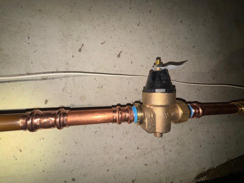 Completed plumbing repair involving the replacement of a worn faucet stem on a bathroom sink fixture with traditional cross-handle design. Successfully installed a 3/4-inch pressure reducing valve (PRV) on the main water supply line using proper copper piping connections with compression fittings to regulate incoming water pressure and protect household plumbing fixtures from potential damage caused by excessive pressure.