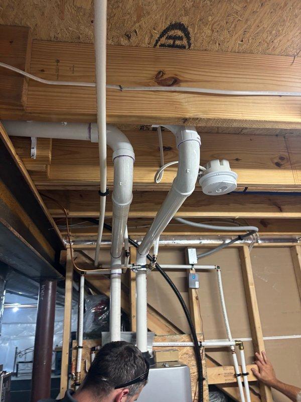 Completed installation of Rinnai RXP199 tankless water heater with RWM200 wireless module in unfinished mechanical space. Installation included mounting unit to OSB wall, running copper supply lines with brass fittings, installing blue expansion tank at floor level, and routing black corrugated flexible venting secured with zip ties. Configured PVC condensate drainage system through ceiling joists with proper support brackets and integrated wireless monitoring module for remote system management.