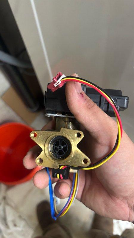 Completed installation of replacement water flow sensor and sensor assembly on tankless water heater unit. Removed failed flow sensor valve assembly and installed new component featuring brass valve body with integrated electronic flow detection system. The replacement assembly includes solenoid actuator with multi-wire harness connection and manual override lever for emergency operation. Properly seated the valve into the unit's compartment, secured all mounting hardware, and reconnected color-coded electrical wiring to the main control board using factory connectors. Verified proper wire routing to prevent interference with other components and ensured all connections were secure. Tested flow sensor operation and confirmed unit functionality upon completion.