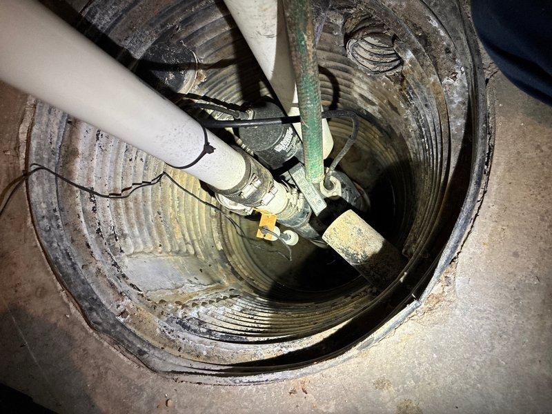Responded to water leak complaint in main floor laundry room. Upon inspection, identified sump pump system as source of moisture issue affecting laundry room wall. Inspected sump basin, pump assembly, discharge piping, and check valve components. Documented existing conditions including water staining patterns on basin walls and proper pump installation with PVC discharge lines. Verified laundry appliances and surrounding areas for additional moisture concerns. Photographed sump pump system and laundry room configuration for service records.