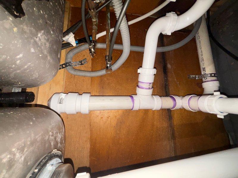 Responded to reported water leak from kitchen sink. Upon inspection, identified leak originating from deteriorated connections at the garbage disposal unit and compromised drain assembly beneath the sink cabinet. Replaced faulty rubber couplings on the disposal unit and reconfigured the PVC drainage system with new fittings and proper sealing. Applied PVC primer and cement to all new connections to ensure watertight installation. Tested all connections under full water pressure to verify leak resolution. System is now functioning properly with no active leaks detected.