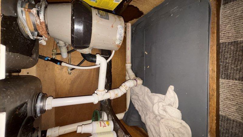 Responded to reported water leak from kitchen sink. Upon inspection, identified leak originating from deteriorated connections at the garbage disposal unit and compromised drain assembly beneath the sink cabinet. Replaced faulty rubber couplings on the disposal unit and reconfigured the PVC drainage system with new fittings and proper sealing. Applied PVC primer and cement to all new connections to ensure watertight installation. Tested all connections under full water pressure to verify leak resolution. System is now functioning properly with no active leaks detected.