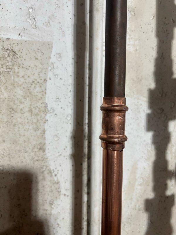 Responded to reported leaking copper pipe in basement. Upon inspection, identified deteriorated section of copper piping with visible corrosion and oxidation damage below the shutoff valve. Replaced compromised pipe section using press-fit coupling connection method. Installed new copper pipe segment with modern press-style fitting featuring ridged dual-ring design to ensure secure, leak-free connection. Verified valve assembly integrity and tested system for proper operation and water-tight seal upon completion.