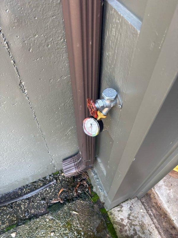Conducted on-site assessment of existing 10-year-old gas water heater located in basement for replacement estimate. Evaluated 50-gallon gas water heater installation, documenting current plumbing connections including copper supply lines, flexible connectors, and pressure regulation components. Inspected exterior gas line infrastructure with pressure gauge and valve assembly mounted on building exterior. Photographed existing installation showing water heater positioned in basement utility area with exposed ceiling joists, copper piping network, PVC ventilation ductwork, and concrete block foundation walls. Assessed all connection points, shut-off valves, and system components to prepare comprehensive estimate for 50-gallon gas water heater replacement while current unit remains operational.