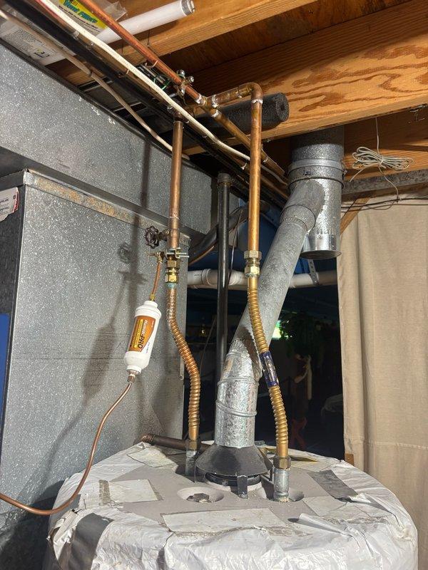 Conducted on-site assessment of existing 10-year-old gas water heater located in basement for replacement estimate. Evaluated 50-gallon gas water heater installation, documenting current plumbing connections including copper supply lines, flexible connectors, and pressure regulation components. Inspected exterior gas line infrastructure with pressure gauge and valve assembly mounted on building exterior. Photographed existing installation showing water heater positioned in basement utility area with exposed ceiling joists, copper piping network, PVC ventilation ductwork, and concrete block foundation walls. Assessed all connection points, shut-off valves, and system components to prepare comprehensive estimate for 50-gallon gas water heater replacement while current unit remains operational.