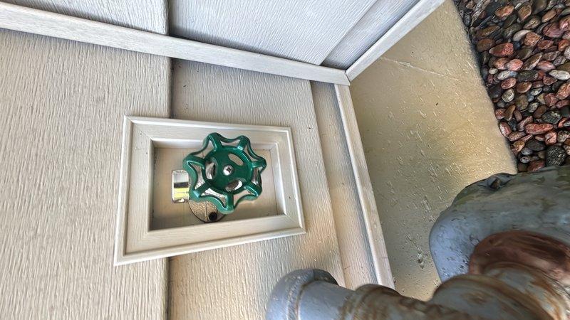 Responded to service call for leaking exterior hose bib. Upon arrival, inspected outdoor water spigot mounted in recessed box on exterior wall and confirmed active leak at valve assembly. Removed damaged brass spigot and assessed supply line condition, noting corrosion on existing vertical pipe. Installed new chrome-plated hose bib with green wheel-style handle in recessed wall box. Connected replacement valve to water supply line and secured all fittings. Tested new installation for proper operation and verified no leaks present. Exterior faucet now functioning correctly with full shutoff capability restored.