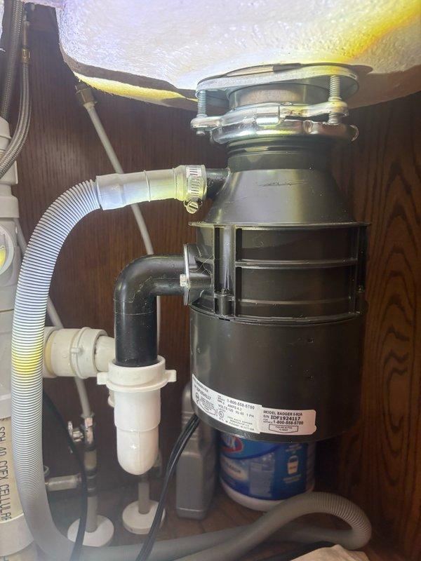 Responded to callback for garbage disposal that was humming but not operating after previous service visit. Upon inspection, found Whirlpool disposal unit jammed and unable to rotate freely. Manually freed impeller assembly using allen wrench access port at bottom of unit, removed obstruction, and verified proper rotation. Tested disposal operation under running water to confirm full functionality and proper drainage through P-trap assembly. Unit now operates normally without humming or binding.