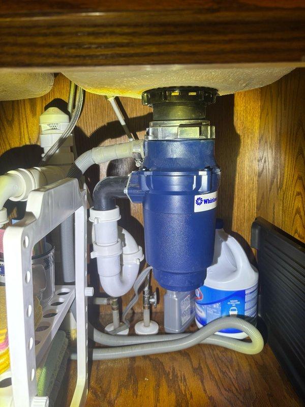 Responded to callback for garbage disposal that was humming but not operating after previous service visit. Upon inspection, found Whirlpool disposal unit jammed and unable to rotate freely. Manually freed impeller assembly using allen wrench access port at bottom of unit, removed obstruction, and verified proper rotation. Tested disposal operation under running water to confirm full functionality and proper drainage through P-trap assembly. Unit now operates normally without humming or binding.