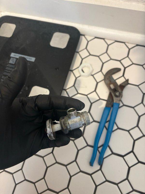 Responded to reported toilet leak in bathroom. Upon arrival, diagnosed faulty angle stop valve supplying water to toilet fixture. Shut off main water supply and removed defective chrome-plated angle stop valve showing mineral deposits and signs of deterioration at compression fittings. Replaced valve with new unit, ensuring proper thread seal and compression connections. Removed toilet tank lid to inspect internal flush mechanism for additional leak sources. Verified all tank components functioning properly with no signs of internal leakage. Reinstalled hardware, restored water supply, and tested system under full pressure to confirm complete resolution of leak. All connections verified watertight with no visible dripping or seepage detected.