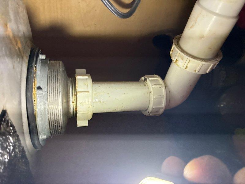 Responded to service call for leak under kitchen sink. Upon inspection, identified leak at metal drain assembly connection point where it meets the PVC P-trap configuration. Orange-brown discoloration and staining visible around the metal drain fitting indicated active water seepage at the connection joint. Inspected all compression fittings, coupling nuts, and rubber gaskets throughout the drain assembly. Tightened connections and verified proper seal at the metal-to-plastic transition point. Confirmed P-trap assembly was properly aligned and all washers were seated correctly. Tested drain system for leaks and verified repair was successful.