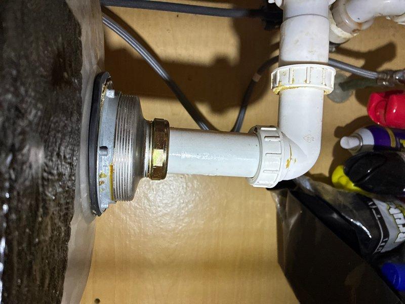 Responded to service call for leak under kitchen sink. Upon inspection, identified leak at metal drain assembly connection point where it meets the PVC P-trap configuration. Orange-brown discoloration and staining visible around the metal drain fitting indicated active water seepage at the connection joint. Inspected all compression fittings, coupling nuts, and rubber gaskets throughout the drain assembly. Tightened connections and verified proper seal at the metal-to-plastic transition point. Confirmed P-trap assembly was properly aligned and all washers were seated correctly. Tested drain system for leaks and verified repair was successful.