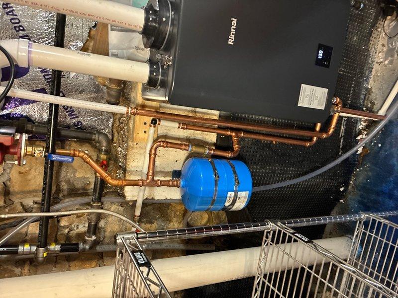 Completed installation of Rinnai RX199 tankless water heater for domestic hot water and NTI FTVN110 boiler system for radiant floor heating. Relocated tankless water heater from original boiler location to exterior wall closet with venting routed through window opening. Connected gas supply line from existing main line at new tankless location and established cold water feed directly from water main. Routed hot water discharge to tie into existing hot water distribution system and configured condensate drain line to discharge at sump pump location. Relocated recirculating pump to new mechanical room housing tankless unit.

Removed existing boiler system and installed replacement NTI FTVN110 boiler with new connection ports integrated to existing radiant floor heating lines. Identified corrosion buildup on circulator pump shut-off valves during removal process and replaced deteriorated valves with new components before reinstalling pump assembly. Installed expansion tank and completed a