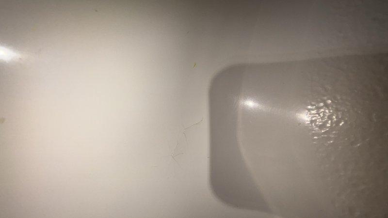 Responded to report of water leaking from upstairs shower through to first floor ceiling. Upon inspection, identified hairline crack in bathtub basin as source of leak. Crack located on interior surface of tub was allowing water to seep through porcelain and penetrate subfloor during shower use. Documented condition of drain assembly and cracked porcelain surface with photographs. Recommended tub replacement or professional refinishing to properly seal crack and prevent continued water intrusion and potential structural damage to ceiling below.