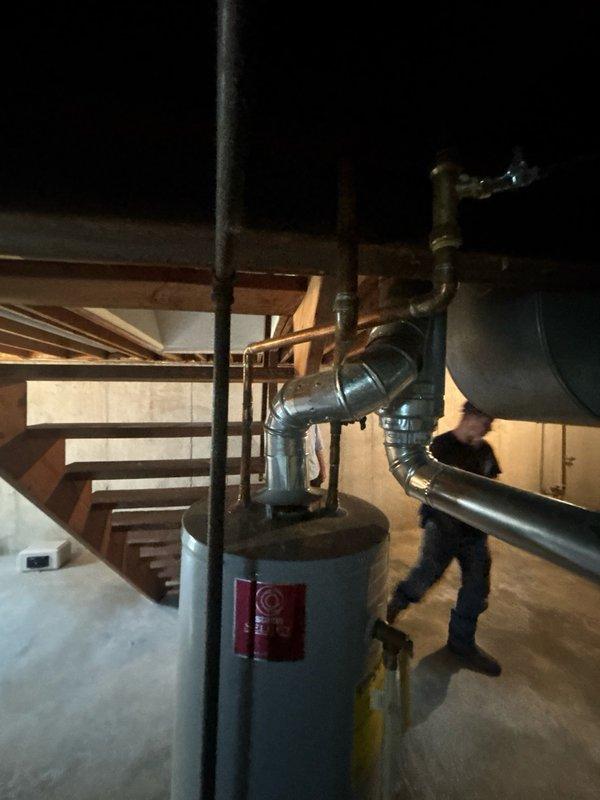 Completed comprehensive assessment of 10-year-old residential water heater located in basement mechanical room. Evaluated existing unit's operational status, inspected copper supply lines with shut-off valves, verified proper venting configuration including black flue pipe and metallic ductwork connections, and examined mounting location on concrete floor between structural support beams. Documented current plumbing infrastructure, valve accessibility, and ventilation system for water heater replacement estimate.