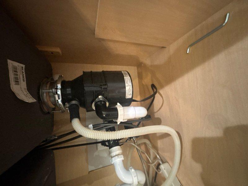 Responded to reported leak under kitchen sink. Upon inspection, identified leak source in the under-sink plumbing assembly connected to the garbage disposal unit. Examined the PVC drain configuration, disposal mounting hardware, and associated drain connections. Tightened loose connections at the disposal drain outlet and P-trap assembly. Verified all plumbing connections were secure and properly sealed. Tested system for leaks by running water through the sink and disposal unit. Confirmed repair successful with no active leaking observed.
