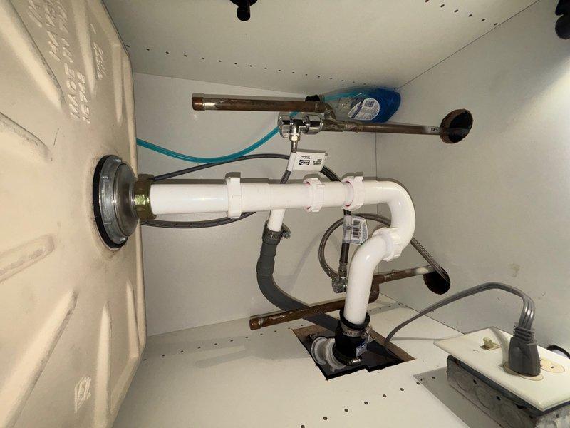 Responded to reported water leak in kitchen and bathroom areas. Upon inspection, identified leaking supply line connection at wall-mounted fixture showing visible rust staining and moisture damage on surrounding white surface. Tightened threaded metallic fitting and secured flexible supply hose with hose clamp to eliminate leak at connection point. Inspected under-sink plumbing infrastructure in cabinet, examining PVC drain trap assembly, multiple pipe joints, and supply line connections. Verified all connections were properly secured and leak-free. System tested and confirmed operational with no active leaks present at time of service completion.