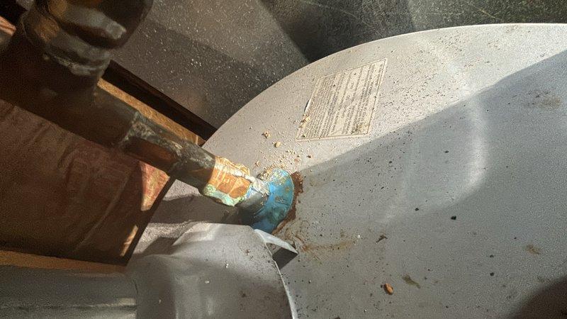 Responded to service call for leaking water heater. Upon arrival, inspected 9-year-old tanked water heater unit and confirmed active leak condition. Visual assessment revealed significant corrosion and oxidation on copper supply piping and connections at top of tank, with green and brown patina indicating advanced deterioration. Blue plastic fitting showed signs of age-related wear. Tank exterior displayed accumulated debris and dust consistent with unit age. Documented existing conditions with photographs showing corroded inlet piping and overall tank condition. Discussed findings and replacement options with customer given age of unit and extent of corrosion damage to plumbing connections.