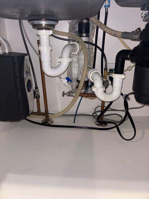 Completed comprehensive plumbing renovation including installation of Puronics 4-stage reverse osmosis system with water softener and customer-supplied toilet with new wax ring seal. Performed extensive under-sink reconfiguration by removing existing garbage disposal unit, installing customer-supplied instant hot water dispenser, and re-piping drain lines to accommodate new layout. Replaced all five supply stops and upgraded copper water supply lines to poly tubing for improved durability and flexibility. Installed Korky fill valve and flapper repair kit in toilet tank to ensure proper flush operation. All connections tested and verified leak-free with proper drainage confirmed throughout the system.