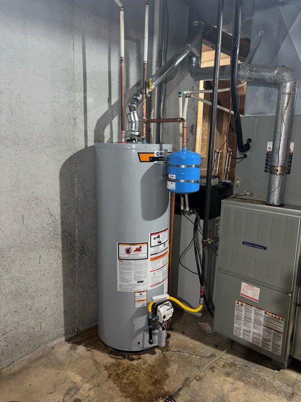 Completed installation of a 50-gallon gas-fired water heater in basement utility area. Unit was positioned on concrete floor and connected to existing gas supply line using flexible yellow connector for code compliance. Installed copper supply piping to top of unit along with thermal expansion tank mounted on cold water inlet line to protect against pressure buildup in closed plumbing system. Connected proper venting using black plastic piping routed upward for exhaust gases. Verified all gas connections for leaks, tested temperature and pressure relief valve operation, and confirmed proper water flow through hot water distribution system. Installation meets current plumbing codes and manufacturer specifications.