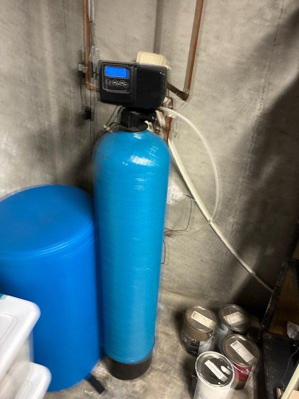 Completed routine plumbing maintenance visit inspecting water treatment system and associated plumbing connections. Verified water softener with digital control head and copper piping connections were operating properly, with all components including secondary tank and flexible tubing in good working condition.