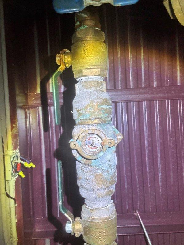 Responded to emergency water leak under stairwell where water was actively spewing from corroded brass piping, requiring building-wide water shutoff. Upon inspection, identified severely corroded brass pipe assembly and pressure reducer valve with extensive verdigris patina and compromised threaded connections. Repaired failed connection point, restored water service to building, and documented existing corrosion on vertical pipe assembly and pressure control components for future maintenance consideration.