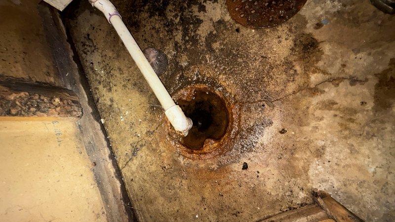 Responded to HVAC recall notice regarding water discharge from floor drain in basement utility area. Upon arrival, inspected floor drain and surrounding concrete surfaces, which exhibited extensive rust-colored staining, deterioration, and water damage radiating outward from drain opening. White PVC drainage pipe observed extending to drain connection point. Concrete floor and walls showed significant moisture exposure, discoloration, and aging consistent with long-term water infiltration. Documented existing conditions including heavily stained drain grate, mottled concrete surfaces with brown and gray discoloration, visible cracks, and worn areas throughout utility space. Area assessed for drainage issues and potential sources of water accumulation at floor drain location.