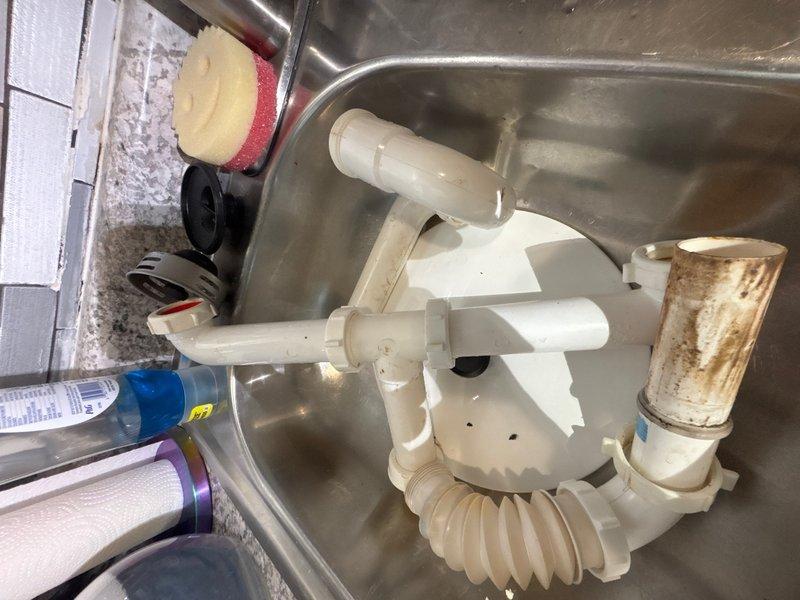 Responded to emergency water leak in kitchen caused by loosened drain pipes beneath sink. Upon arrival, inspected P-trap assembly and discovered improper connections allowing water to escape onto floor. Disassembled white PVC P-trap configuration, cleaned all connection points, and reassembled drain system with proper alignment and secure fittings. Verified all compression connections were tightened to manufacturer specifications. Tested drainage system by running water through sink to confirm leak was eliminated and proper flow was restored. Left work area clean and all plumbing components functioning correctly.