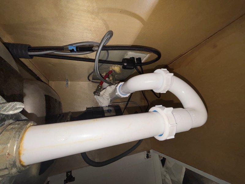 Responded to emergency water leak in kitchen caused by loosened drain pipes beneath sink. Upon arrival, inspected P-trap assembly and discovered improper connections allowing water to escape onto floor. Disassembled white PVC P-trap configuration, cleaned all connection points, and reassembled drain system with proper alignment and secure fittings. Verified all compression connections were tightened to manufacturer specifications. Tested drainage system by running water through sink to confirm leak was eliminated and proper flow was restored. Left work area clean and all plumbing components functioning correctly.