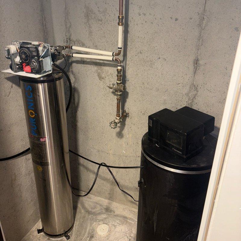 Performed comprehensive tune-up and maintenance service on a 10-year-old Concord water softener system located in basement. Inspected control head functionality, verified proper regeneration cycles, and tested all system components including the black brine tank and stainless steel mineral tank. Examined plumbing connections including copper supply lines showing mineral deposits and white PEX distribution piping with brass fittings. Cleaned control valves, checked salt levels in brine tank, and confirmed proper water flow through the treatment system. All components found to be operating within normal parameters, and system returned to full service.