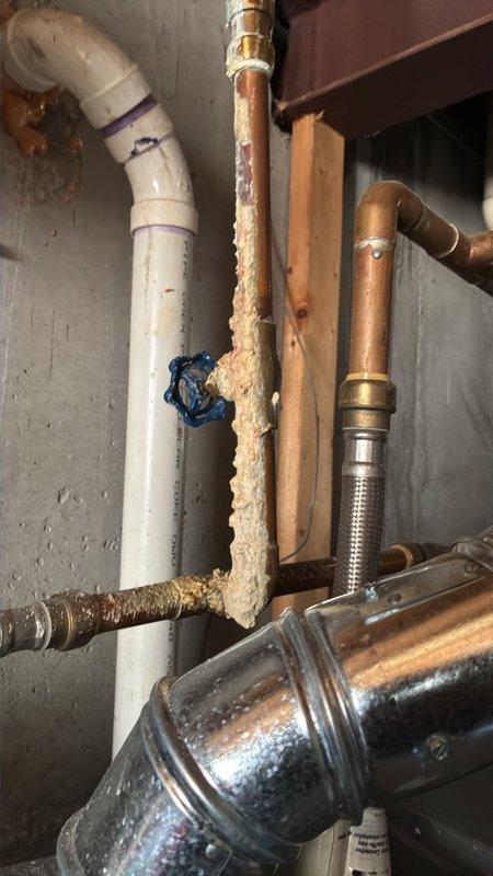 # Plumbing Maintenance Visit

Conducted comprehensive plumbing inspection in basement utility area, documenting extensive mineral buildup and corrosion on vertical copper piping system. Photographed deteriorated copper pipes showing significant white crusty deposits and oxidation, along with existing PVC, brass fittings, and flexible connector installations mounted to structural framing. Assessment revealed advanced pipe corrosion requiring monitoring or potential replacement to prevent future leaks or system failure.