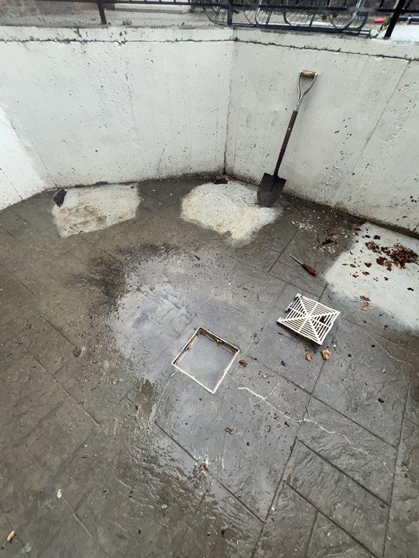 # Patio Drain Cleaning - Slow Drainage Issue Resolved

Responded to service call for patio drain experiencing significantly reduced flow rate. Upon arrival, inspected square drain basin installed in concrete patio floor showing visible signs of debris accumulation and standing water around drain fixture. 

Performed thorough assessment of drainage system and identified blockage causing slow water evacuation. Cleared obstruction from drain line using appropriate drain cleaning equipment and techniques. Removed accumulated organic debris, sediment, and buildup from drain basin and surrounding area that was contributing to poor drainage performance.

Tested drain flow after clearing blockage to verify proper water evacuation and confirm restoration of normal drainage function. Patio drain now operating at full capacity with no standing water remaining in basin area.