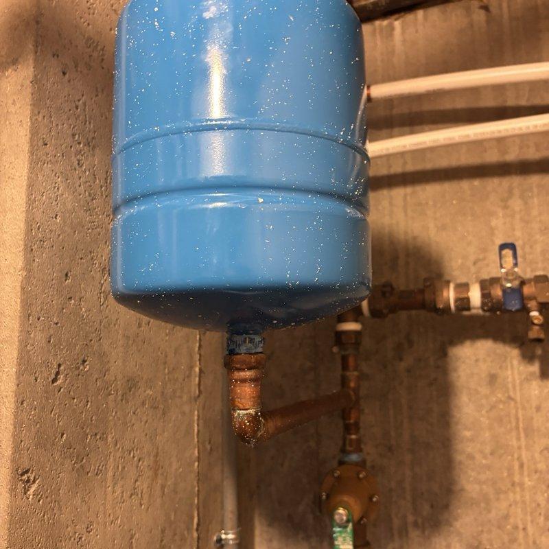Responded to emergency service call for water heater with blown gasket. Upon arrival, water supply had already been shut off by customer to prevent further flooding. Inspection revealed significant internal corrosion and rust accumulation around the tank base and drain assembly, indicating advanced deterioration of the unit. The pressure tank system showed external condensation and corroded copper piping connections, suggesting ongoing moisture issues within the plumbing system. Assessed the extent of damage to determine whether gasket replacement was viable or if full unit replacement would be required due to the severity of internal corrosion observed at the tank bottom and drainage components.
