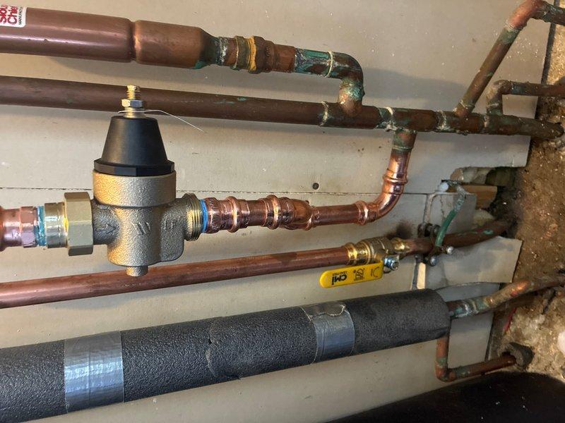 Installed new 3/4" pressure reducing valve (PRV) on main water line. Removed existing main shut off valve that was positioned too close to the whole-house water supply tee, preventing proper PRV installation. Installed new ball valve in upward-facing orientation to accommodate PRV assembly. Rerouted and repiped copper water line from new PRV back into main supply line feeding the house, ensuring proper water pressure regulation throughout the system.