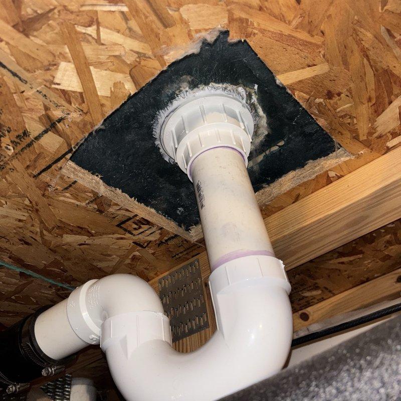 Completed shower drain replacement in residential bathroom, removing existing worn drain assembly and installing new chrome-plated drain cover with debris screen. Accessed P-trap configuration from below through subfloor, verifying proper drainage and trap seal functionality with white PVC piping and fittings properly secured through OSB decking.