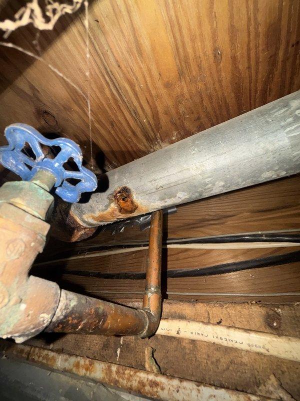 Responded to a burst pipe emergency in the basement affecting the kitchen drain line. Upon inspection, discovered severely corroded copper piping with extensive oxidation and rust damage that had compromised the pipe integrity, resulting in a complete failure of the line. The affected section exhibited significant patina buildup, black deposits, and weakened areas where corrosion had eaten through the pipe wall.

Removed the damaged section of copper drain line and replaced it with new copper piping, ensuring proper fitting connections and secure joints. Installed a new gate valve with blue handle for future maintenance accessibility. All connections were properly soldered and pressure-tested to verify leak-free operation. Confirmed proper drainage flow through the kitchen line and verified no additional leaks or compromised sections in the surrounding plumbing infrastructure. The replacement piping was securely mounted to the floor joists to prevent future stress on the connections. S