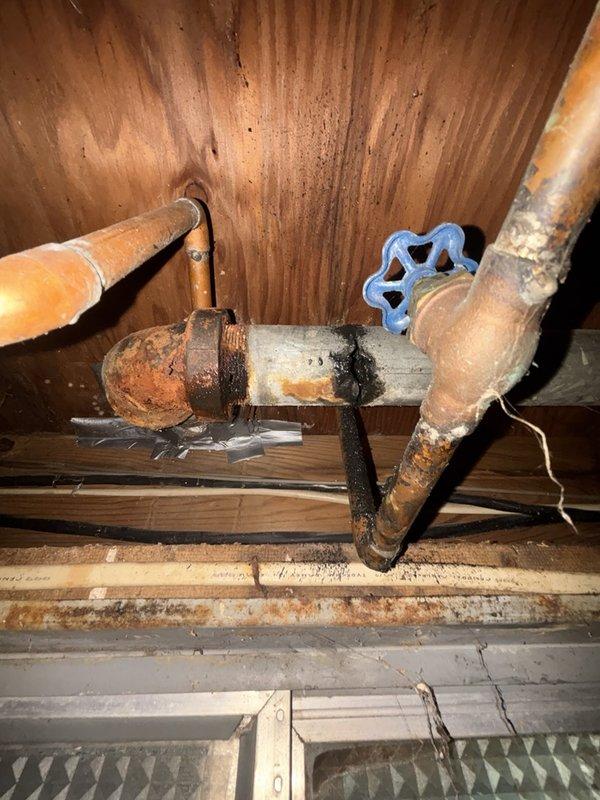 Responded to a burst pipe emergency in the basement affecting the kitchen drain line. Upon inspection, discovered severely corroded copper piping with extensive oxidation and rust damage that had compromised the pipe integrity, resulting in a complete failure of the line. The affected section exhibited significant patina buildup, black deposits, and weakened areas where corrosion had eaten through the pipe wall.

Removed the damaged section of copper drain line and replaced it with new copper piping, ensuring proper fitting connections and secure joints. Installed a new gate valve with blue handle for future maintenance accessibility. All connections were properly soldered and pressure-tested to verify leak-free operation. Confirmed proper drainage flow through the kitchen line and verified no additional leaks or compromised sections in the surrounding plumbing infrastructure. The replacement piping was securely mounted to the floor joists to prevent future stress on the connections. S
