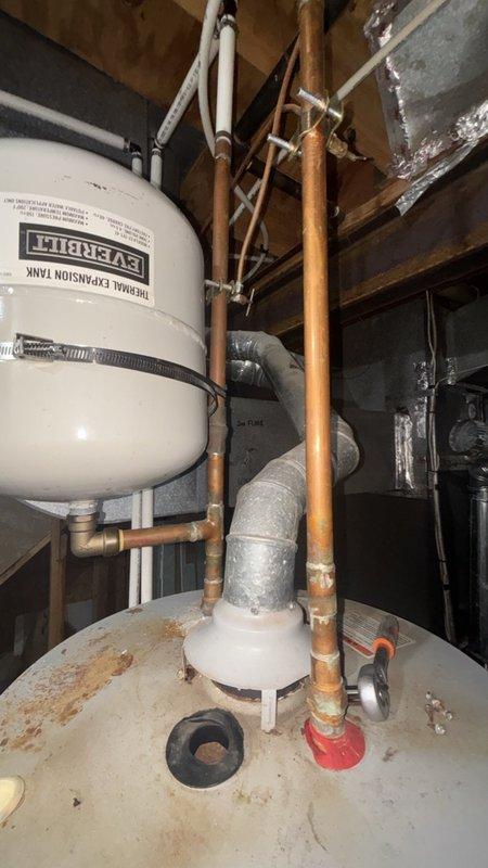 Responded to service call for reported water heater leak at base of unit in basement. Upon arrival, conducted thorough inspection of tanked water heater system and associated plumbing components. Examined white cylindrical water heater tank, expansion tank, copper piping connections, and all valves for signs of active leakage. Observed significant rust staining and discoloration on top crown surface of water heater tank, indicating previous moisture exposure. Inspected base of unit, copper supply lines, pressure relief valve, drain valve, and all threaded connections for source of reported leak. Checked expansion tank mounting and connections. Evaluated condition of oxidized copper piping throughout system. Documented existing rust damage and wear patterns on tank surfaces. Photographed equipment condition and plumbing configuration for service records. Provided assessment of unit condition and discussed repair options with customer to address leaking issue and prevent further water da