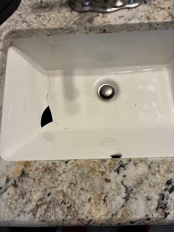 Completed comprehensive plumbing inspection of residential property, documenting condition of water supply system components including pressure tank, brass fittings, and valves in utility space. Identified and photographed significant damage to bathroom sink basin, including large crack with missing ceramic material requiring replacement, and documented all findings for customer review.
