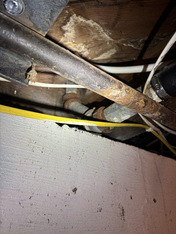 Responded to a clogged kitchen drain line service call. Upon inspection, discovered severely corroded metal drain piping beneath the kitchen sink showing significant rust deterioration and structural compromise. Assessed the existing plumbing configuration, which included a double-basin setup with garbage disposal unit, white PVC drain assemblies, and P-trap connections. Documented the extensive corrosion on the main drain line and confirmed that the existing metal piping has deteriorated beyond repair. Advised that complete drain line replacement will be necessary to restore proper drainage function and prevent future failures. Photographed the corroded pipe sections in the crawl space area and under-sink plumbing assembly for documentation purposes.